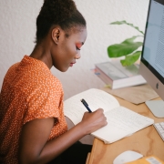 woman writing at desk in front of her computer